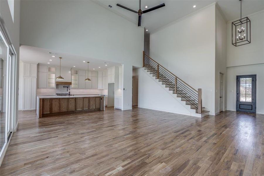 Unfurnished living room featuring ornamental molding, an inviting chandelier, light wood-type flooring, and a high ceiling