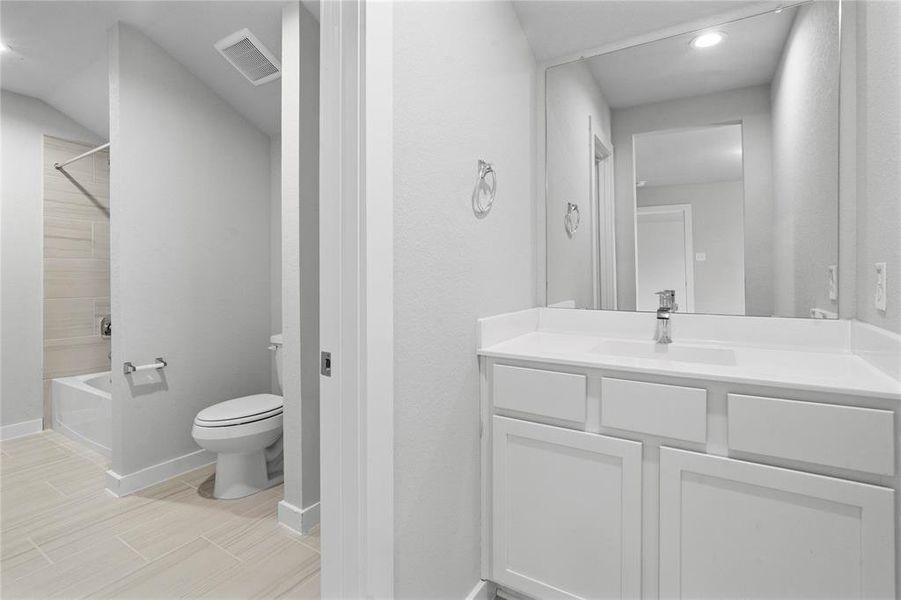 Secondary bath is a jack and jill bathroom featuring tile flooring, bath/shower combo with tile surround, white stained wood cabinets, beautiful light countertops, mirror, sleek fixtures and modern finishes.