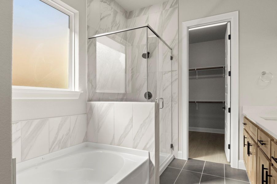 Full bath with vanity, a bath, a marble finish shower, dark tile patterned floors, and a walk in closet Full bath with vanity, a bath, a marble finish shower, dark tile patterned floors, and a walk in closet