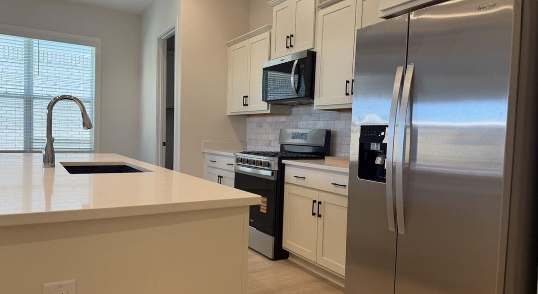 Kitchen with stainless steel appliances, backsplash, light wood-style flooring, light stone countertops, and white cabinetry