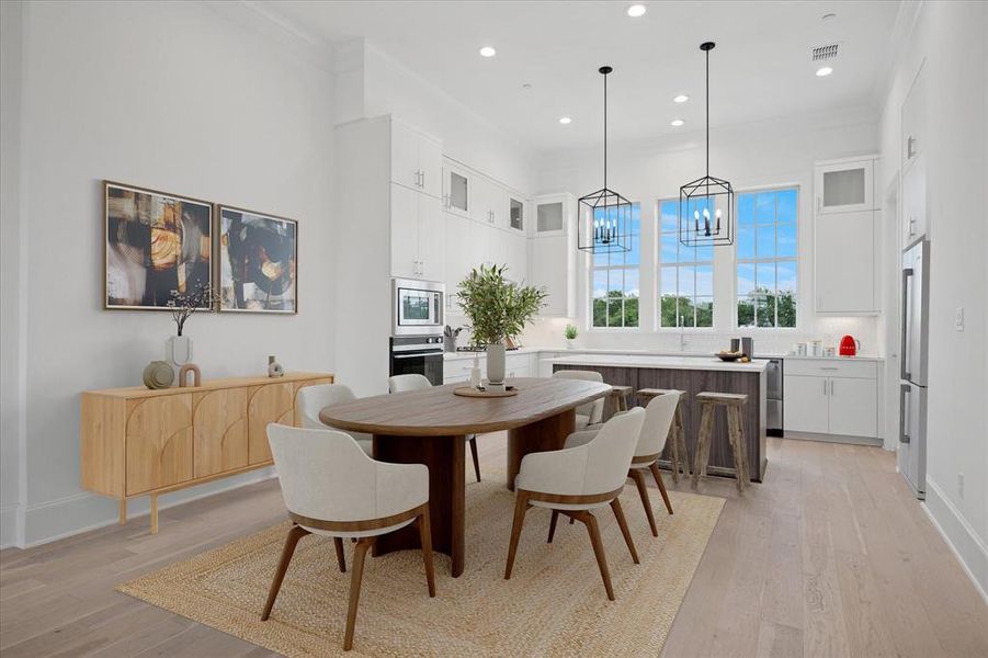 Dining area featuring light wood finished floors, ornamental molding, hanging lights, and a high ceiling