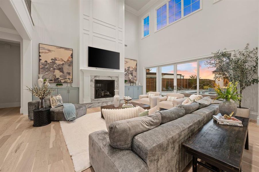 Living room featuring ornamental molding, light wood-style floors, a high ceiling, and a premium fireplace Living room featuring ornamental molding, light wood-style floors, a high ceiling, and a premium fireplace