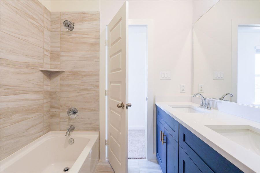 Modern bathroom featuring a spacious walk-in glass shower, elegant blue vanity with gold handles, and a large mirror. Bright, clean design with light tile flooring and walls.