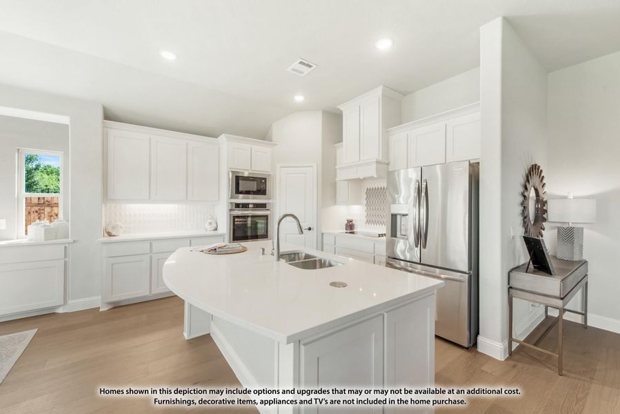 Kitchen with white cabinets, curved island with sink, stainless steel appliances, and light wood floors