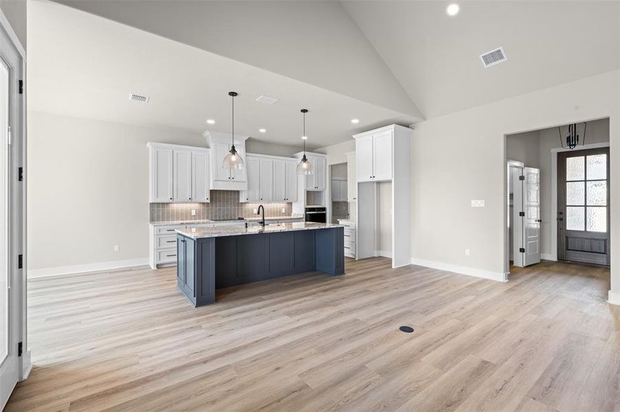 Kitchen with white cabinets, a center island with sink, pendant lighting, light wood finished floors, and high vaulted ceiling
