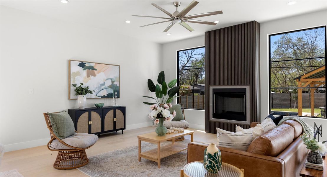 Living room with a large fireplace, wood finished floors, a ceiling fan, and recessed lighting