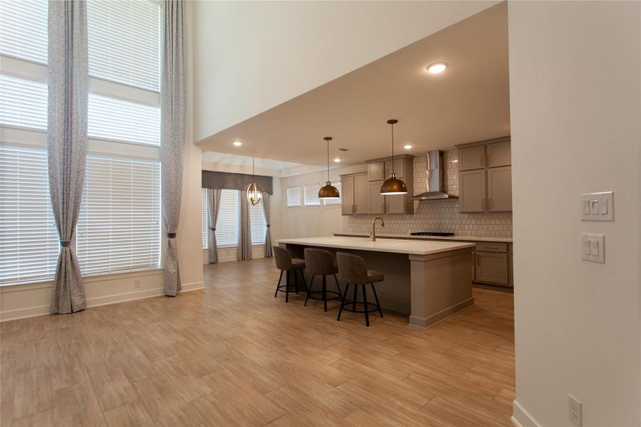 The chef's kitchen anchors the heart of the home with an oversized quartz island, gray shaker cabinets, brass pendants, and built-in stainless appliances. Sightlines stretch straight to the soaring family room, fireplace, and staircase — perfect for entertaining.