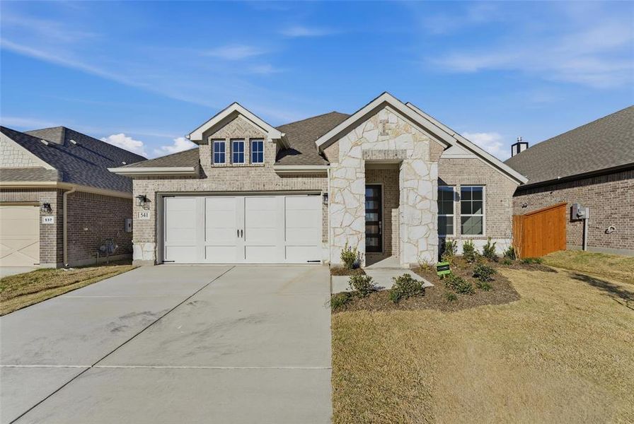 View of front of house with stone siding, brick siding, driveway, a shingled roof, and a front lawn
