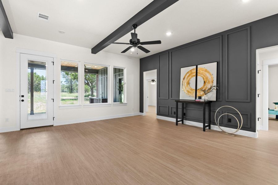 Unfurnished living room with a decorative wall, beam ceiling, ceiling fan, and light wood-style floors