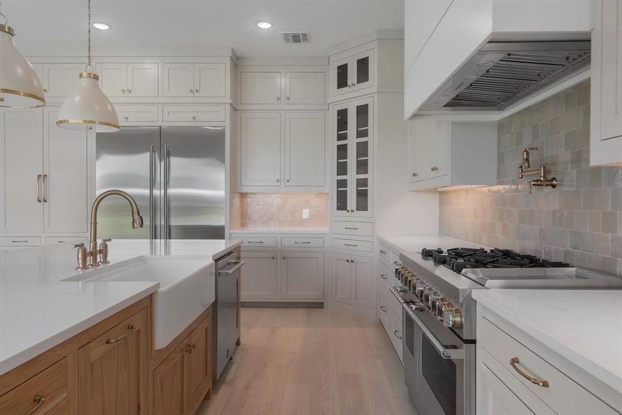 Kitchen with decorative backsplash, high quality appliances, white cabinets, and wall chimney exhaust hood