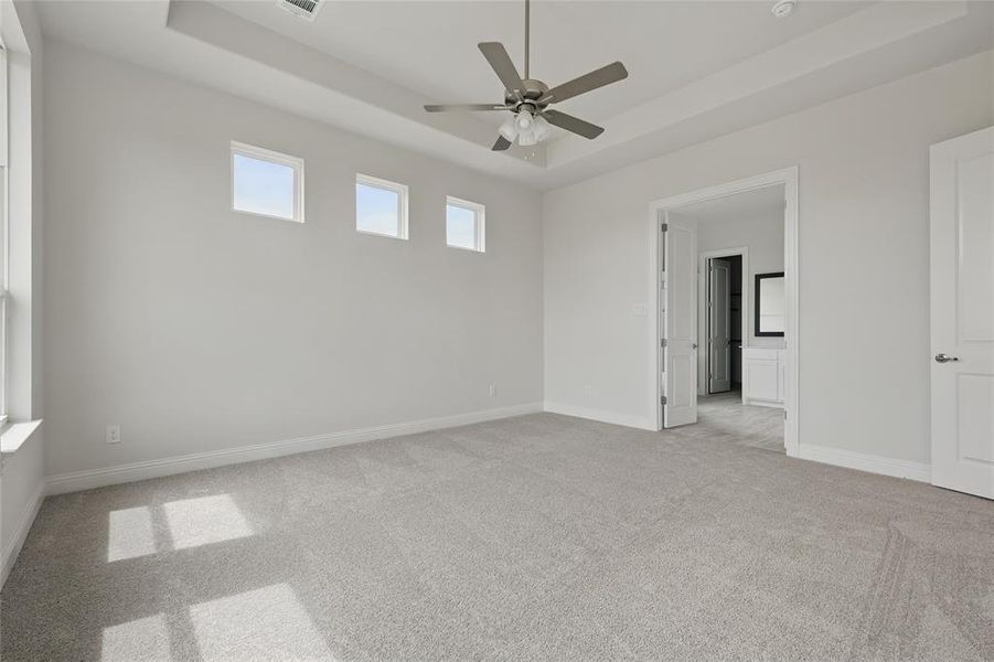 Unfurnished room with a tray ceiling, light colored carpet, ceiling fan, and baseboards