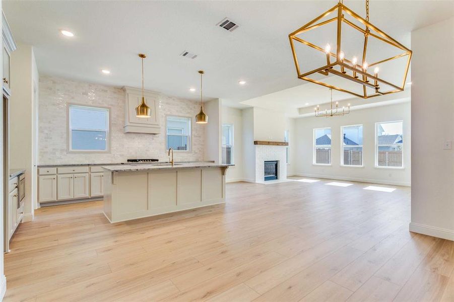 Kitchen featuring hanging light fixtures, light stone counters, light hardwood / wood-style flooring, an island with sink, and a chandelier