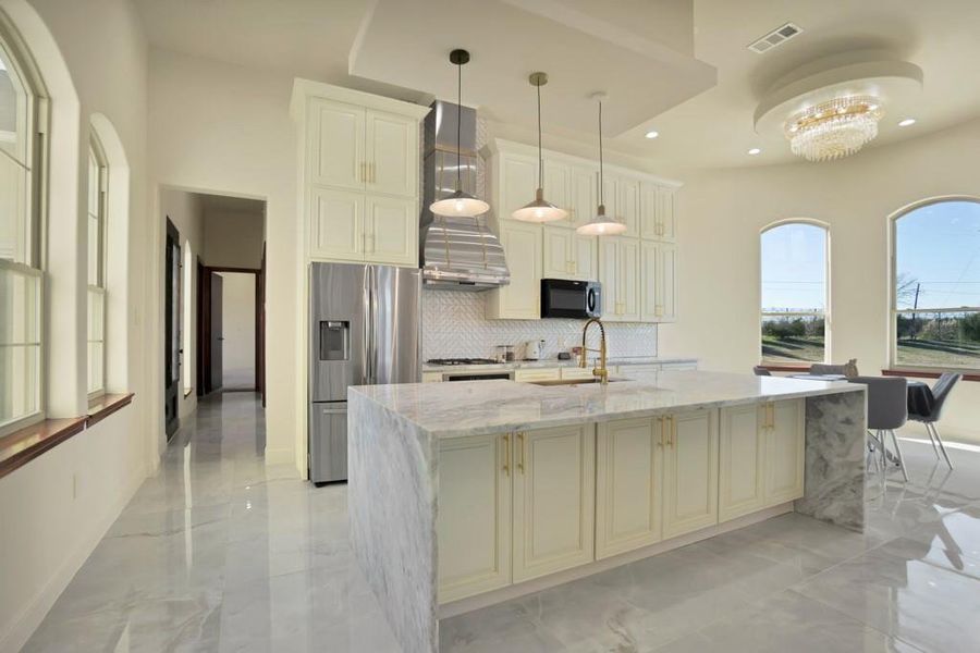 Kitchen with stainless steel refrigerator with ice dispenser, an island with sink, sink, and light stone counters