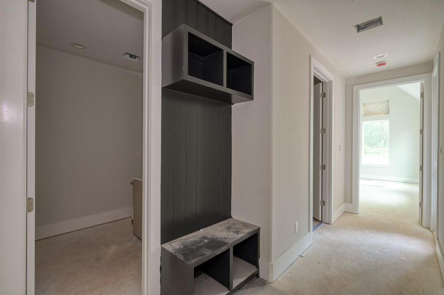 Bright hallway with neutral walls, featuring built-in shelving that leads to laundry and primary suite with natural light filtering in from a large window at the end. Perfect for a modern and organized home.