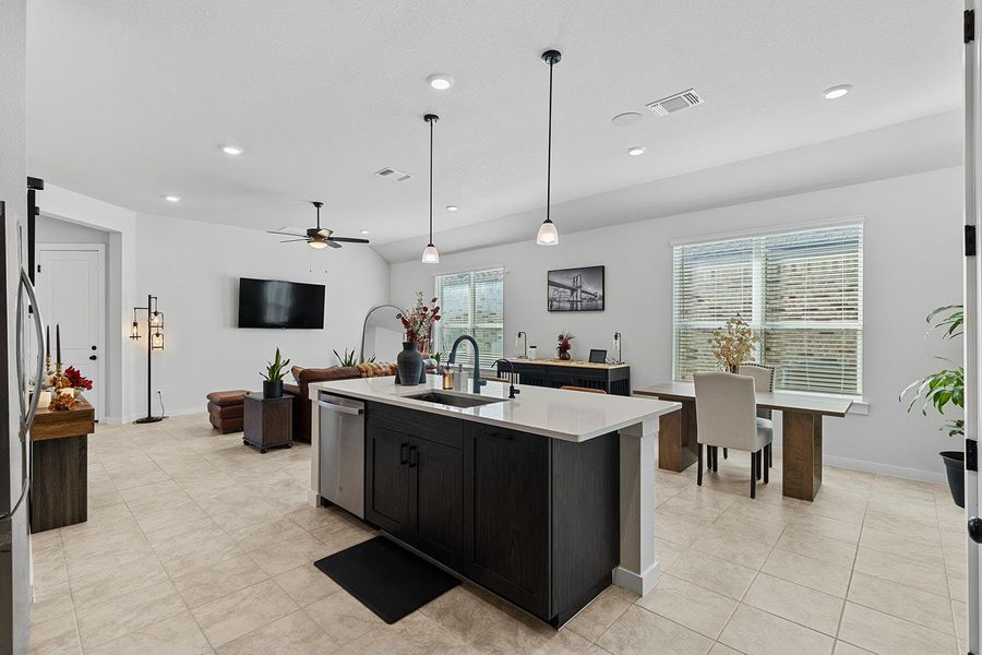 Kitchen featuring decorative light fixtures, a ceiling fan, dark cabinets, a kitchen island with sink, and open floor plan