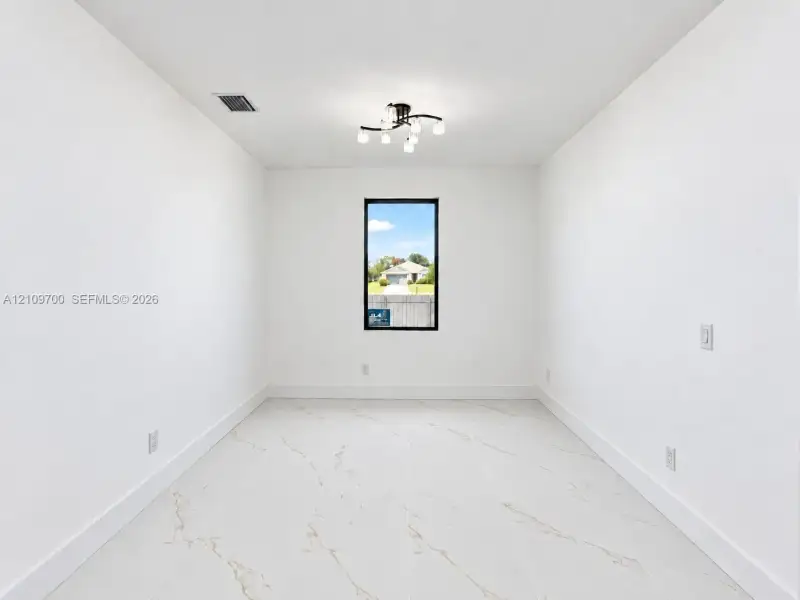 Interior room featuring large-format tile flooring with veining, a modern multi-light fixture, and a vertical window with a dark frame