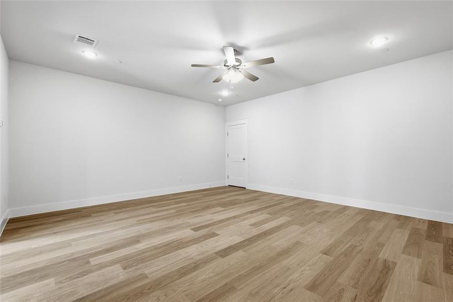 Spacious room featuring light wood-style flooring, white walls, and a ceiling fan with integrated lighting