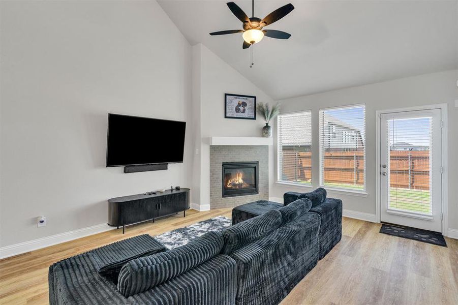Living area featuring vaulted ceilings, wood-finish flooring, a contemporary fireplace with a tiled surround, a ceiling fan, and a glass-paneled exterior door