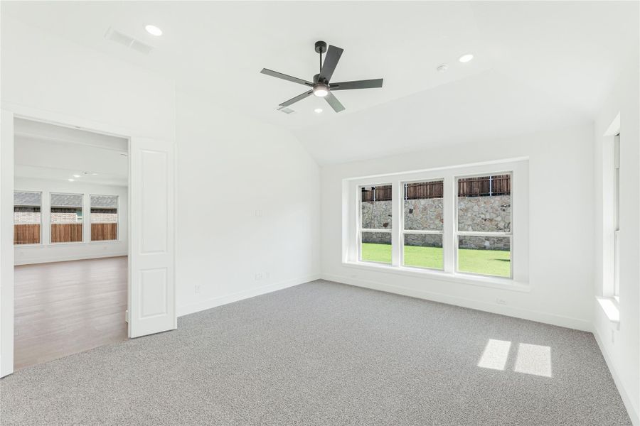 Empty bedroom with vaulted ceiling, ceiling fan, gray carpet, and large window overlooking backyard Empty bedroom with vaulted ceiling, ceiling fan, gray carpet, and large window overlooking backyard