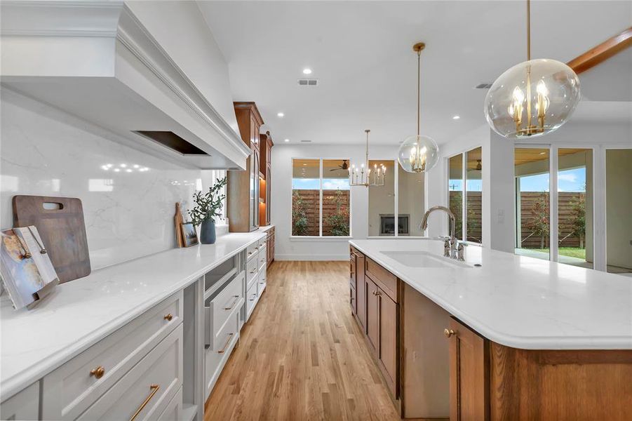 Dual tone kitchen featuring two tone cabinets, a large island, suspended lighting, light wood-style floors, and light stone countertops