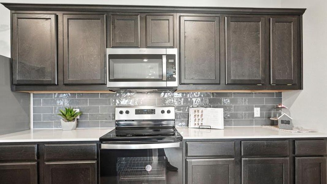Kitchen with stainless steel appliances, tasteful backsplash, dark wood finish cabinets, and light stone countertops Kitchen with stainless steel appliances, tasteful backsplash, dark wood finish cabinets, and light stone countertops