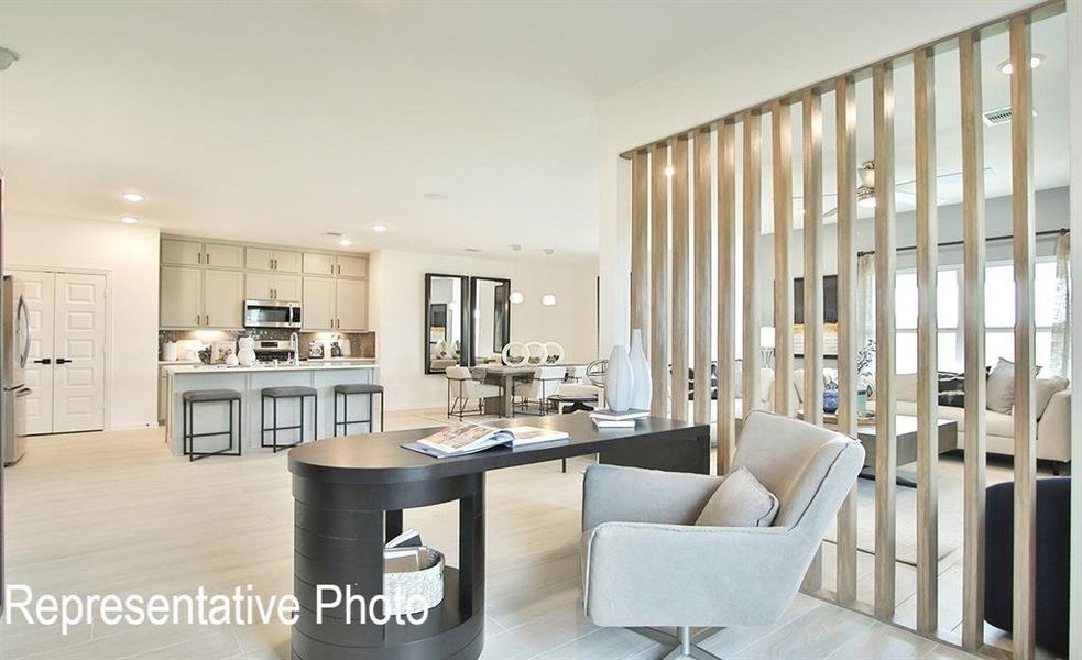 Open-concept interior featuring light wood-finish flooring, a contemporary slatted room divider, recessed lighting, and a kitchen with light gray cabinetry and stainless steel appliances