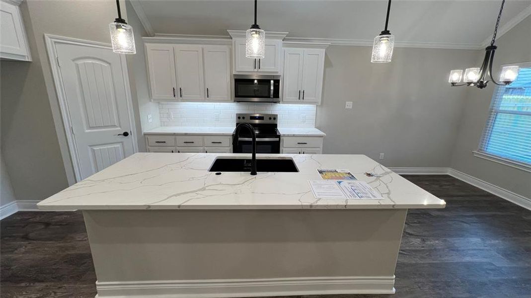 Kitchen with ornamental molding, appliances with stainless steel finishes, white cabinets, and a center island with sink