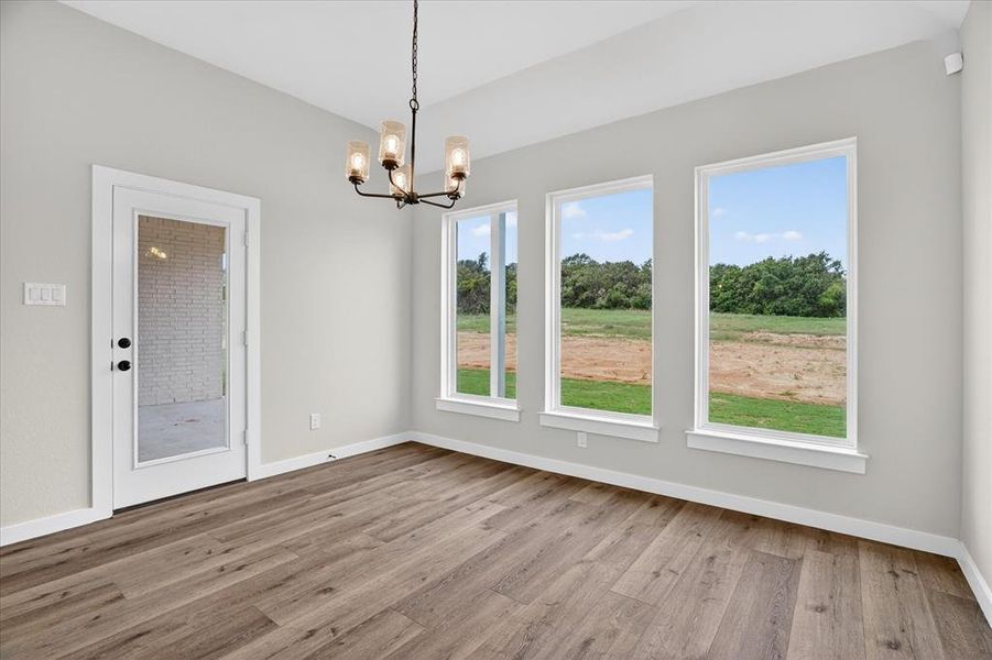 Spacious room featuring wood-finish flooring, light grey walls, and a contemporary chandelier