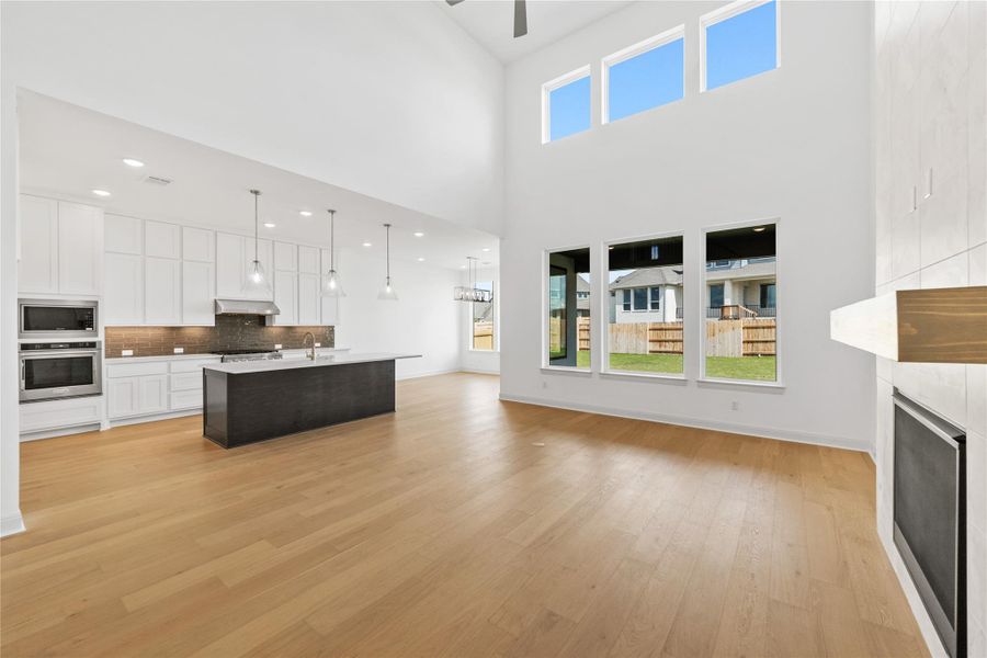 Living room featuring light wood-style flooring, a ceiling fan, a fireplace, and a high ceiling