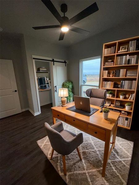 Home office featuring ceiling fan, a barn door, and dark hardwood / wood-style flooring