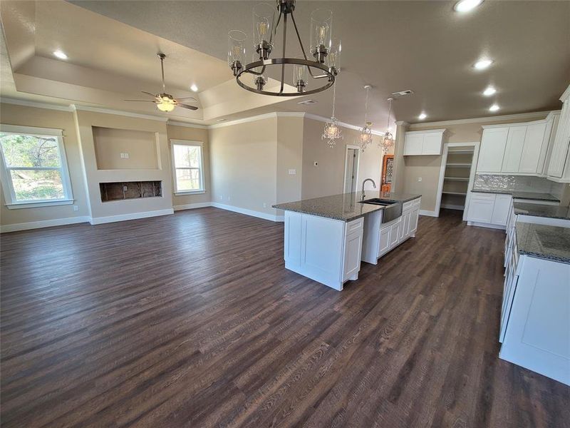 Kitchen with dark wood-type flooring, ceiling fan with notable chandelier, an island with sink, white cabinets, and sink