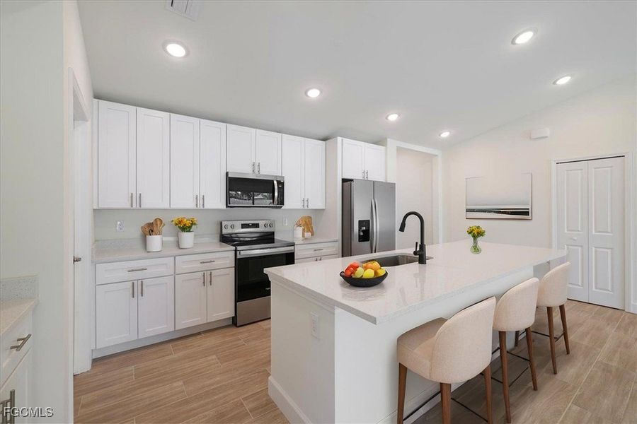 Kitchen featuring stainless steel appliances, wood tiled floors, white cabinetry, a kitchen bar, and a center island with sink