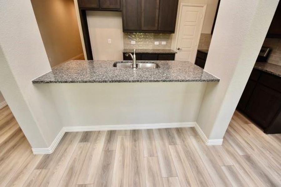 Kitchen featuring stone countertops, dark brown cabinets, a peninsula, and light wood-style floors Kitchen featuring stone countertops, dark brown cabinets, a peninsula, and light wood-style floors