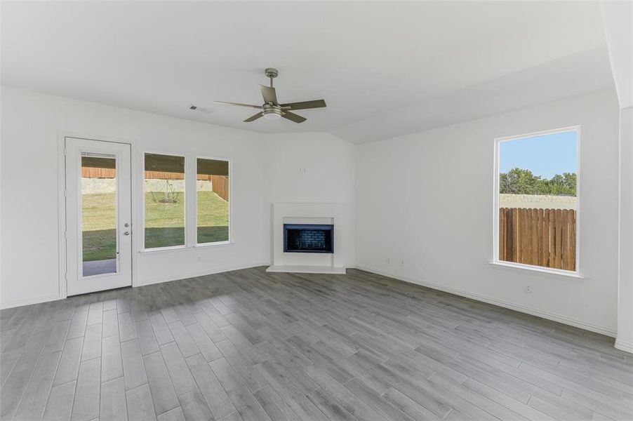 Unfurnished living room with ceiling fan, light wood finished floors, and a fireplace with raised hearth