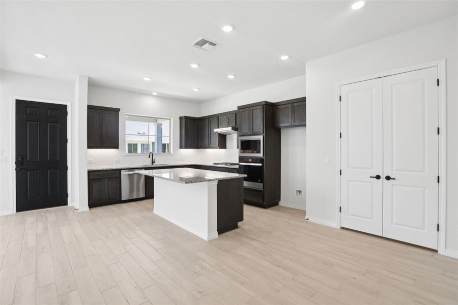 Kitchen with a kitchen island, light wood finished floors, recessed lighting, light stone countertops, and stainless steel appliances