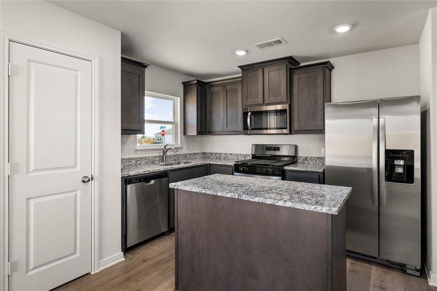 Kitchen with appliances with stainless steel finishes, dark brown cabinets, a center island, light stone counters, and dark wood-type flooring Kitchen with appliances with stainless steel finishes, dark brown cabinets, a center island, light stone counters, and dark wood-type flooring