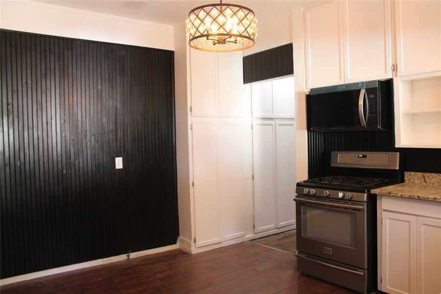 Kitchen with gas stove, white cabinetry, dark wood-type flooring, a chandelier, and light stone counters Kitchen with gas stove, white cabinetry, dark wood-type flooring, a chandelier, and light stone counters