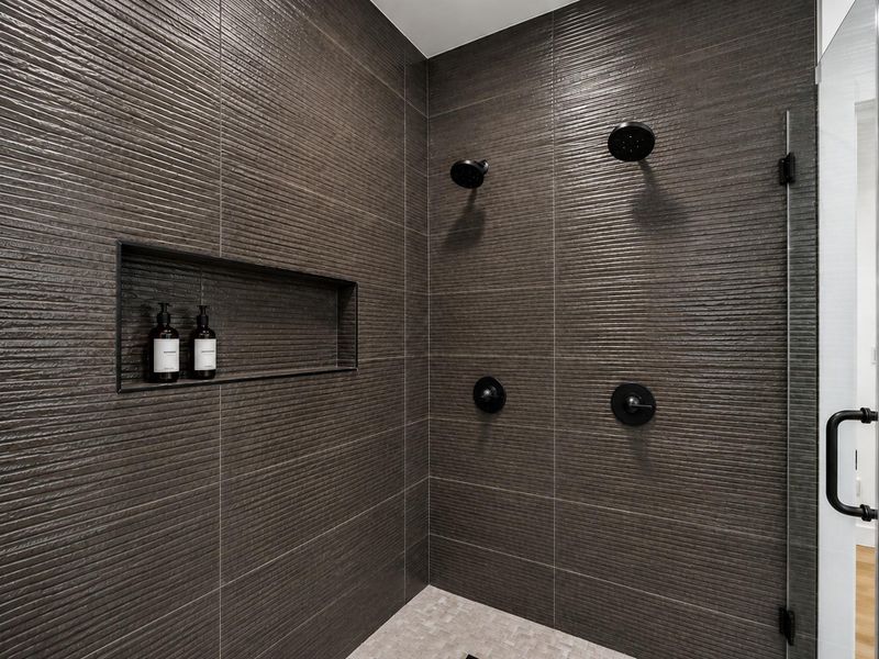 Oversized walk in shower featuring dual showerheads, sleek black fixtures, textured tile, and a built in niche for added convenience.
