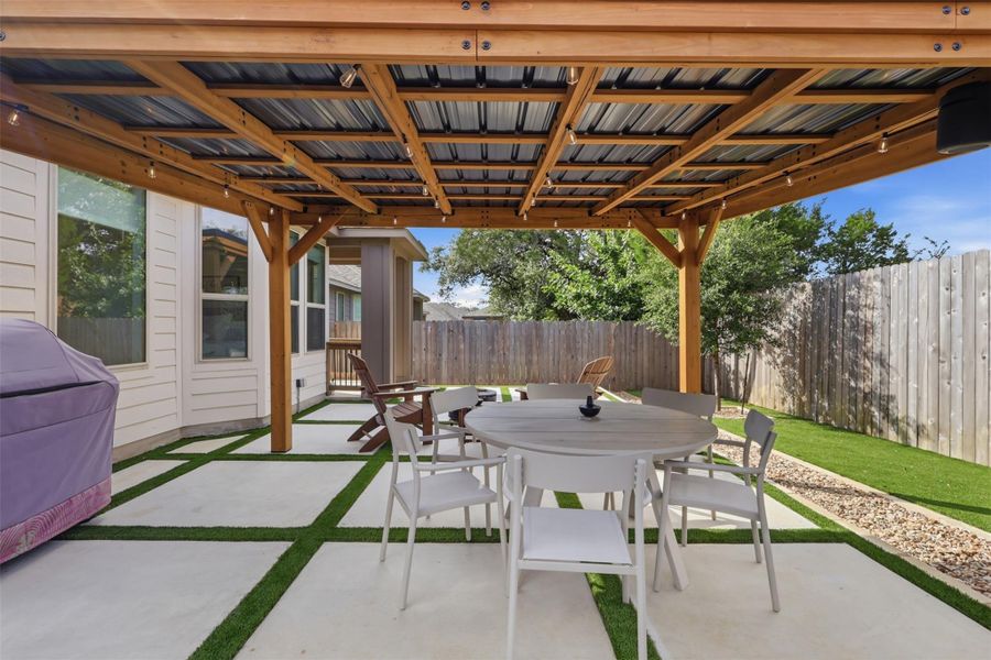 An inviting covered patio features modern pavers inset with grass and a wooden shelter.