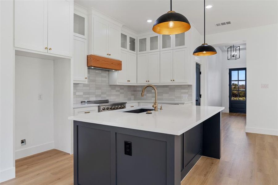 Kitchen with sink, white cabinetry, light hardwood / wood-style flooring, a center island with sink, and decorative light fixtures