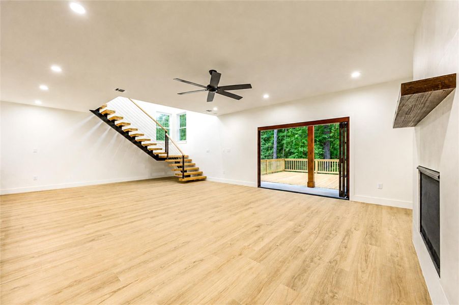Spacious open-concept living area featuring a sleek floating staircase, modern fireplace, and large folding doors perfect for entertaining.