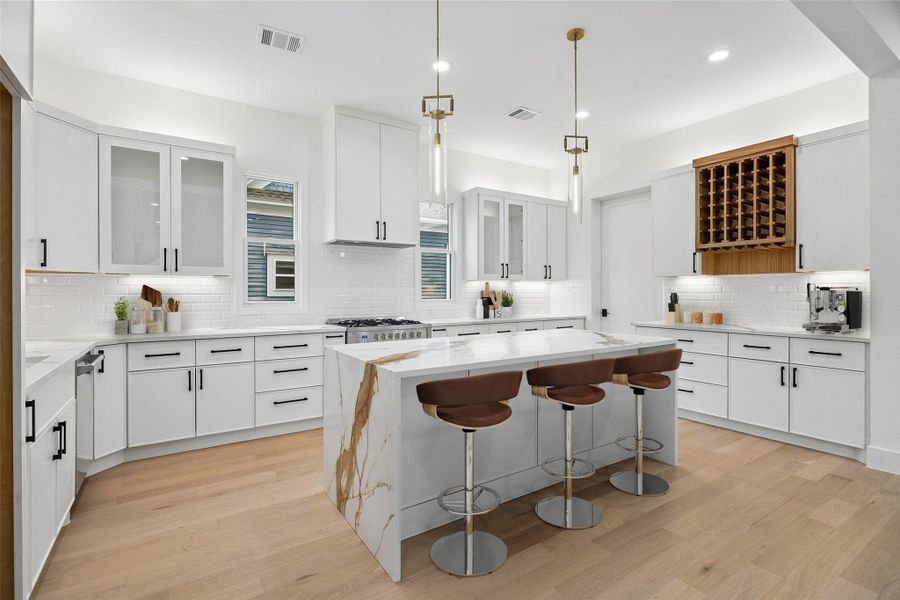 Centered around a waterfall-edge quartz island, the kitchen combines generous prep space, integrated seating, stainless steel appliances, and custom cabinetry within one cohesive design. The surrounding layout allows the kitchen to remain visually connected to both the dining and living areas while maintaining strong functionality for cooking, entertaining, and everyday use. (digitally staged)