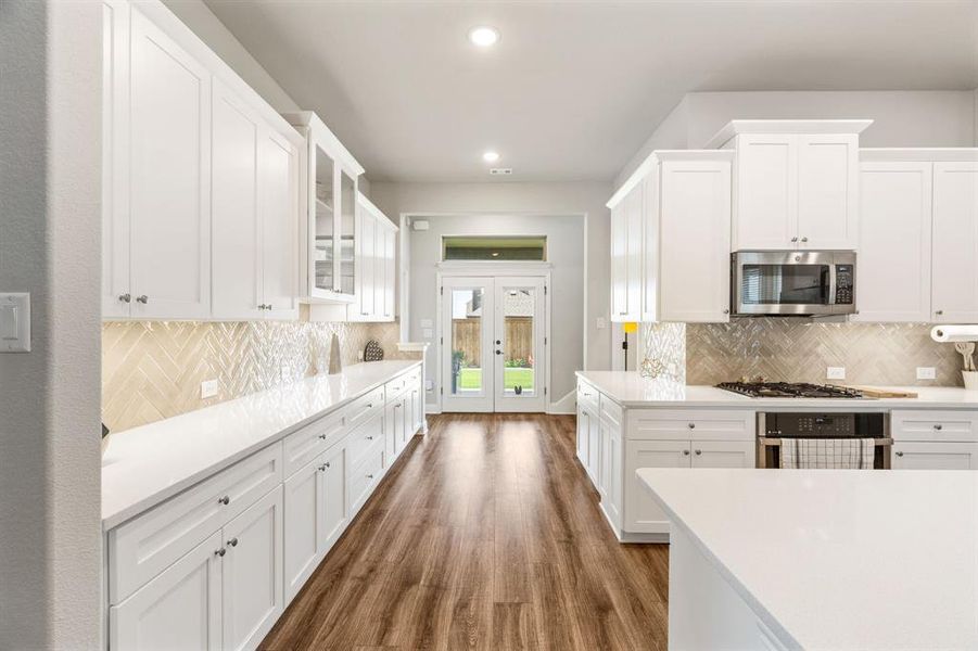 Spacious kitchen featuring extensive white cabinetry, light-toned countertops, and wood-finish flooring Spacious kitchen featuring extensive white cabinetry, light-toned countertops, and wood-finish flooring
