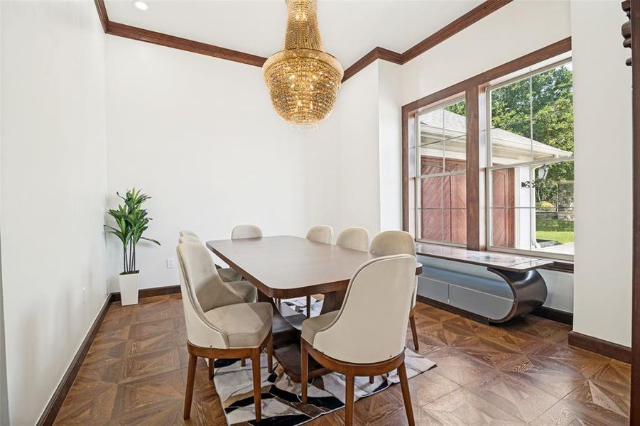 Dining area featuring a prominent chandelier, wood-finish flooring with a geometric pattern, and expansive windows framed by dark wood trim