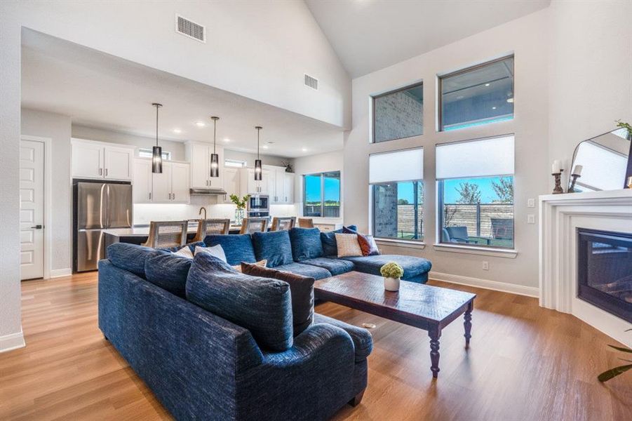 Living room featuring high vaulted ceiling, a glass covered fireplace, light wood-type flooring, and recessed lighting