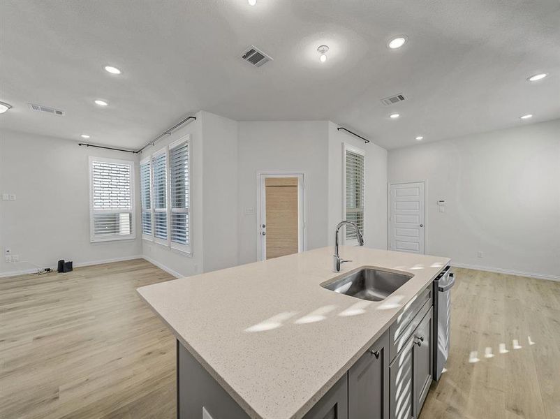 Kitchen featuring light stone countertops, sink, a center island with sink, and light wood-type flooring