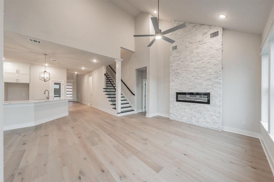 Unfurnished living room with light wood-style floors, a stone fireplace, high vaulted ceiling, stairs, and a ceiling fan