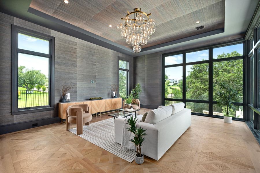 Artfully patterned hardwood flooring grounds a room featuring soaring ceilings and panoramic views of the verdant surroundings.