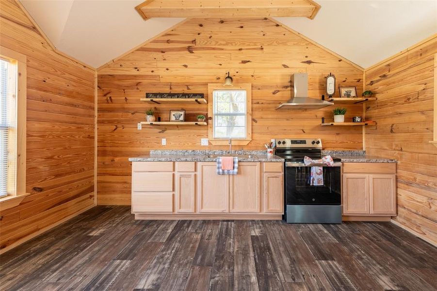 Kitchen featuring wood-paneled walls, vaulted ceilings, laminate wood-finish flooring, light wood cabinetry, and granite-style countertops