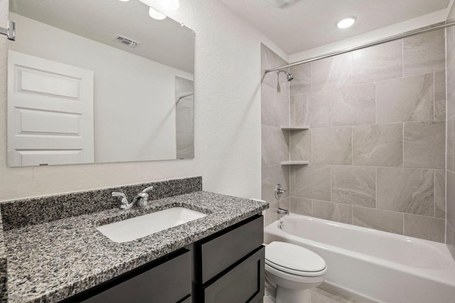 Polished granite counters and matching wall tile elevate this updated bathroom space.